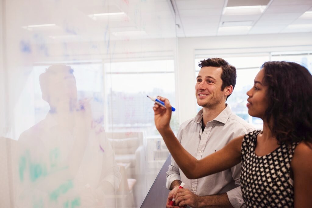 Two colleagues brainstorming on a glass board.