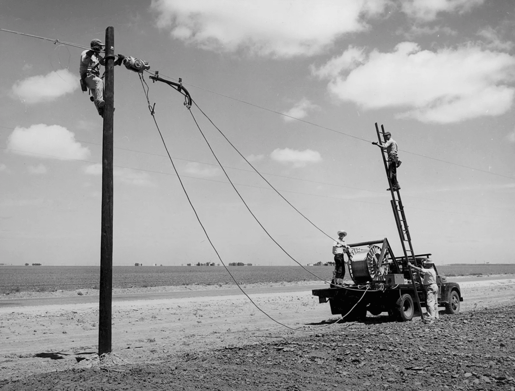 Linemen installing power lines in rural area, 1940s.