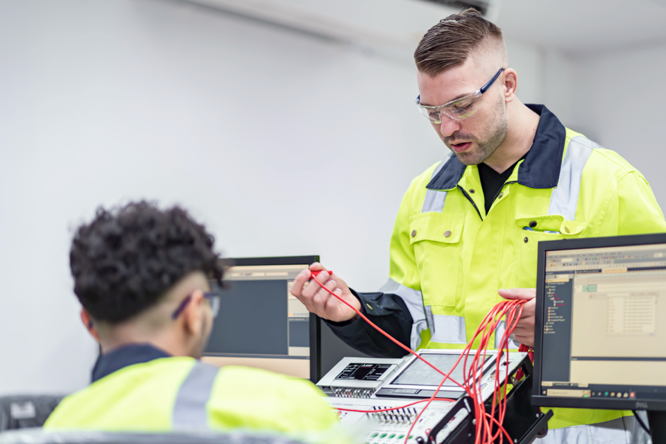 Technician holding red cables beside computer monitors
